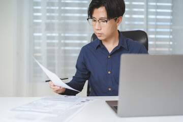 Asian Business man looking at paperwork while using computer laptop when planing about investing or trading on stock market or Bitcoin Cryptocurrency. Businessman work, analyze financial data on desk. - 613368754