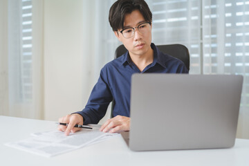 Asian Business man looking at computer laptop when planing about investment on stock market or Bitcoin Cryptocurrency, pointing on paperwork for analysis and checking on financial risk and profit data - 613368772
