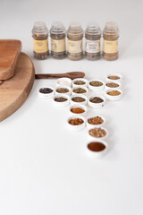 Mesa con diferentes opciones de especias presentadas en tapas, con tablas de madera a un lado y de fondo los contenedores