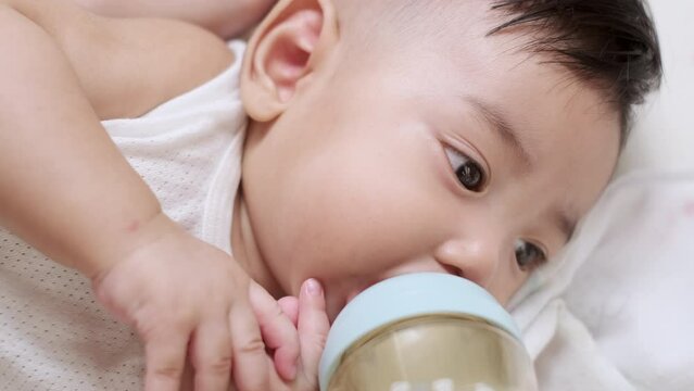 Adorable little Asian baby drinking from baby bottle. Mother holding bottle milk feeding to baby. Concept babies healthcare.