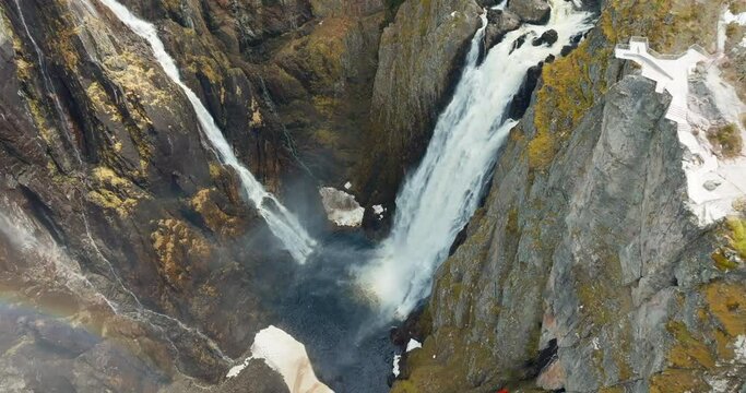 Drone flight over roaring Vøringsfossen waterfall canyon with rainbow in mist