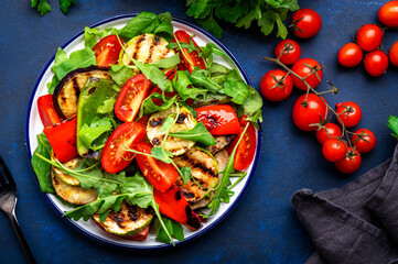 Summer healthy salad with grilled vegetables, paprika, zucchini, eggplant with cherry tomatoes and mixed herbs. Blue table background, top view