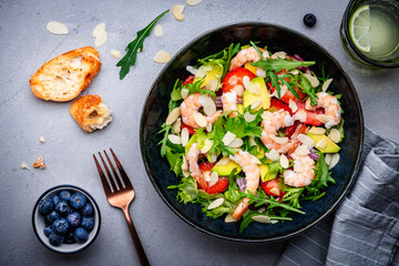 Strawberry, shrimp and herbs salad with arugula, lettuce, avocado and almond slices, gray table. Fresh useful dish for healthy eating. Top view