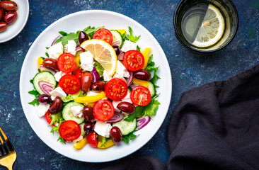 Tasty Greek salad with feta cheese, kalamata olives, tomatoes, paprika, cucumber and onion, healthy mediterranean food. Blue table background, top view