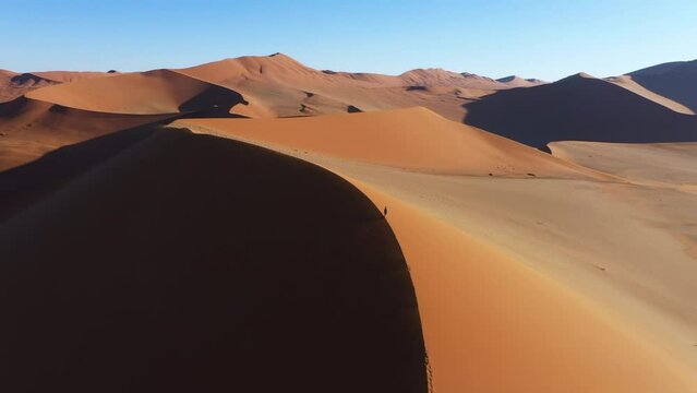 Aerial view around a person on top of a sunny dune in a large desert landscape