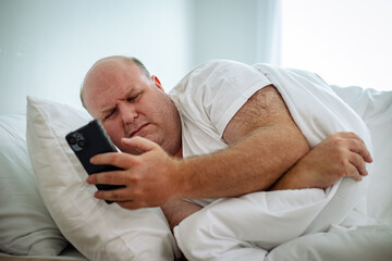 Senior man in white atmosphere switchs the alarm off of his phone. Man sleeping on couch at home...