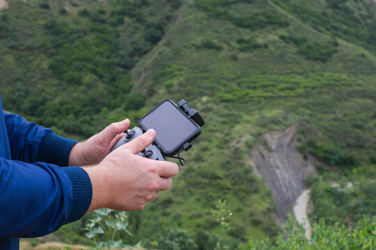Hands of a young man using a drone remote controller  with a phone in mountains