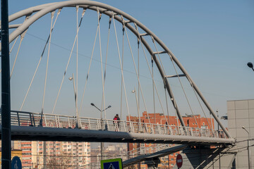 Oval arch of a pedestrian bridge over a road in the city.