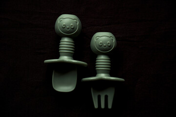 Empty dishes for baby, soft shatterproof tableware for the first feeding, fork and spoon for baby food on black texture background.