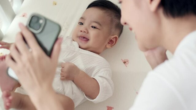 Adorable asian baby and mother video call to father or relatives in a bed. Concept of technology, new generation,family, connection, parenthood