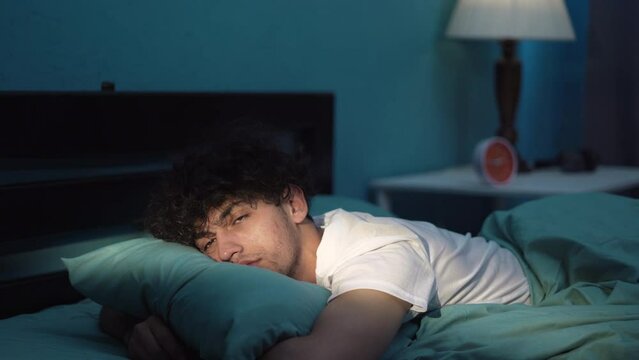 Young man lying in bed late at night trying to sleep suffering insomnia and sleeping disorder