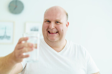 Caucasian white fat man drinks a water in a drinking glass in every morning.