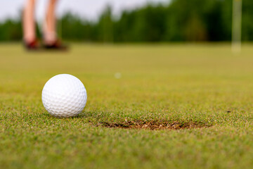 A golfer puts a golf ball on a green golf, the glare in the sun sets in the evening.