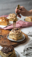 A hand with a fork trying a sweet cinnamon roll with chocolate and some other desserts behind