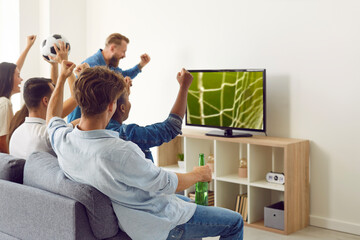 Happy, excited friends watching soccer on TV. Group of young diverse multiracial people sitting on...