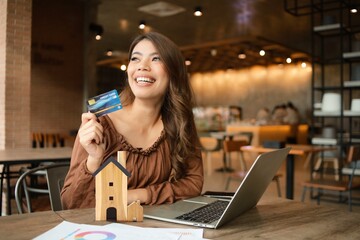 Beautiful Asian woman broker working in cafe, woman with model of house in coffee shop.