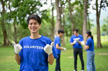 Naklejka premium A happy young Asian male volunteer stands in a public park and shows his thumbs up