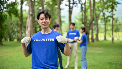 Naklejka premium A happy Asian male volunteer stands in a public park, participating in volunteer work