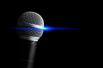 Close up dynamic microphone with blue concert light, isolated on black. Singing, recording, broadcasting, speech concept - 613407779