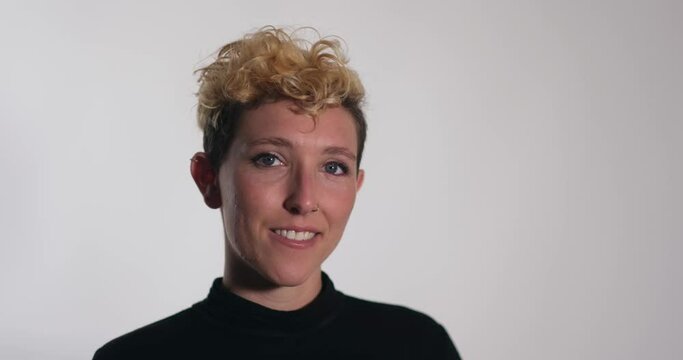 A nonbinary model with curly hair, a fade haircut, and blue eyes smiles for a motion portrait.