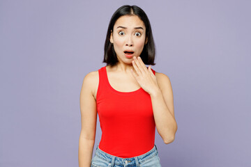 Young shocked scared woman of Asian ethnicity wear casual clothes red tank shirt look camera cover mouth with hand isolated on plain pastel light purple background studio portrait. Lifestyle concept.