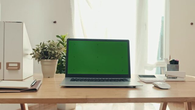 Medium shot of laptop with green chroma key screen on table in office with no people there