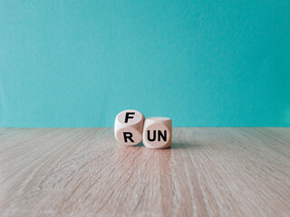 Hand is turning a cube and changes the word Fun to Run. Beautiful wooden table, blue background. Lifestyle concept, copy space.