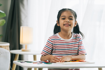 Fototapeta premium Happy asian child girl drawing with colorful pencils in living room at home