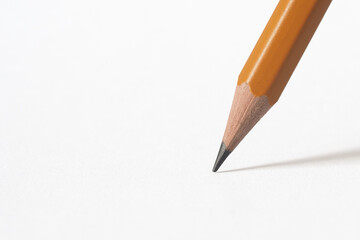 the tip of a wooden pencil casting a shadow on white paper. White backgroud