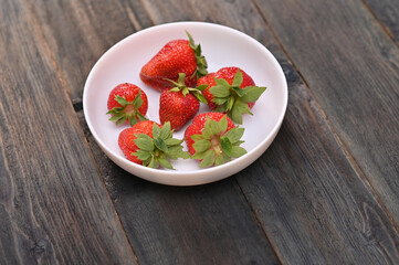 Strawberries in a white plate on a dark wooden background.