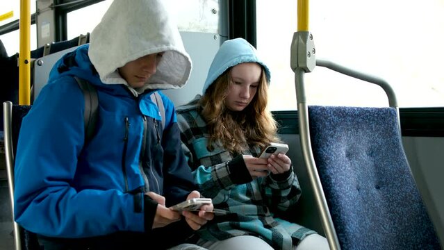 two teenagers in blue clothes sit on bus Canada Vancouver hoods autumn winter spring tracksuits use a mobile phone search for geolocation travel travelers real life