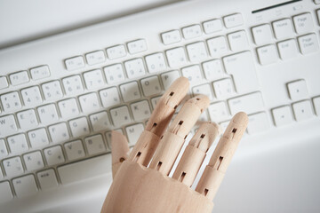 木製のロボットの手の指とパソコンのキーボード
