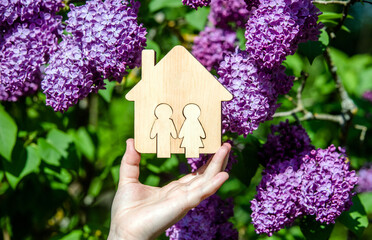 The girl holds the house symbol against the background of blossoming purple lilac
