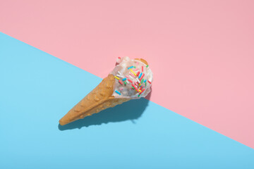 top view of ice cream cone and strewed sprinkles on blue and pink background with hard shadow, summer concept