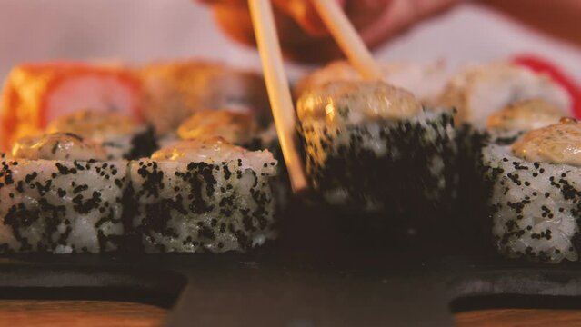 A traditional Japanese seafood meal. Close-up. Chopsticks bert from the black stone plate sushi rolls. Assorted sushi, rolls, Asian food with fresh ingredients on a dark background