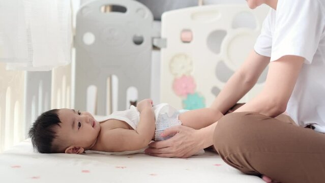 Cute Asian baby wearing clothes by his mother after changing him diaper in nursery at home.  Asian family mother&rsquo;s day concept.