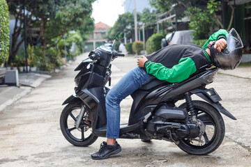 Fototapeta na wymiar online transportation driver is laying on his parked scooter while waiting for an order, feeling tired and sleepy