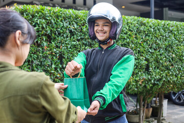 Online taxi driver motorbike wearing green jacket and helmet delivering order to customer