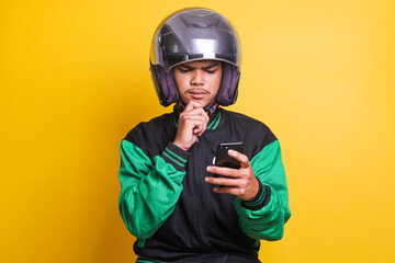 Asian online taxi driver wearing green jacket and helmet using mobile phone while thinking