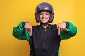 Asian online taxi driver wearing green jacket and helmet pointing fingers down over yellow background