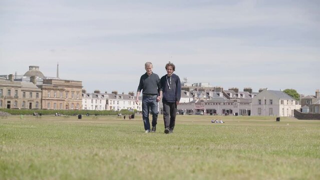 Two gay males with significant age difference walk hand in hand on grass