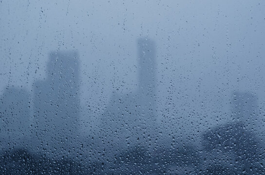 Rain drop on glass window in monsoon season with blurred city buildings background.