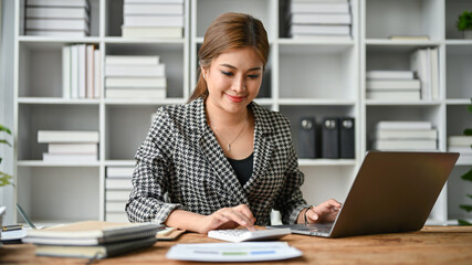 A beautiful Asian businesswoman using a calculator and working on her work on her laptop