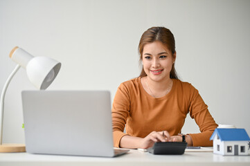 A beautiful Asian woman using a calculator to calculate her house loan at her desk.