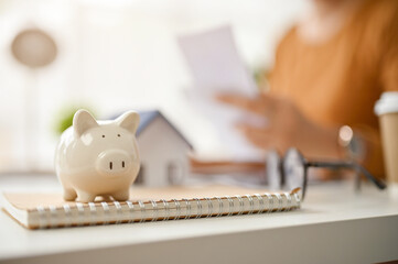 Close-up image of a piggy bank is on table with a female real estate agent working behind.