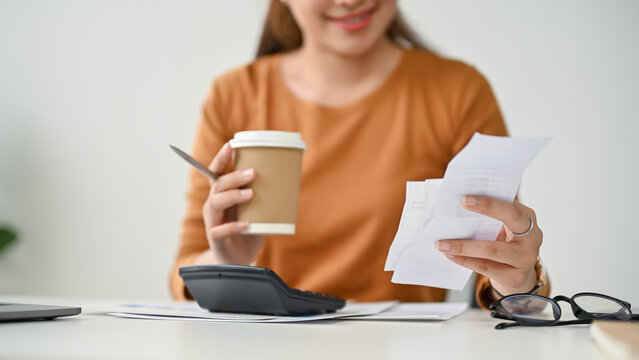 Close-up image of a beautiful Asian woman sipping coffee and checking her bills