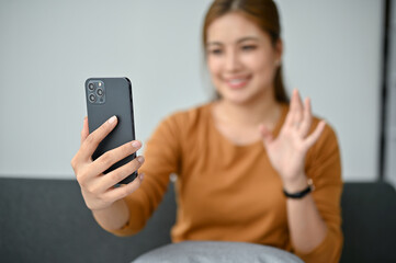 A woman talking with her friends through a video call on her smartphone in the living room.