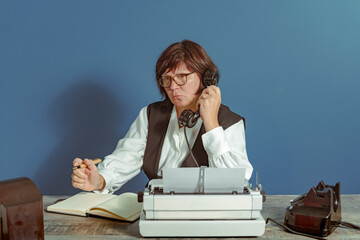 Brunette secretary from the past at work. Vintage concept. Table with telephone and typewriter. - Powered by Adobe