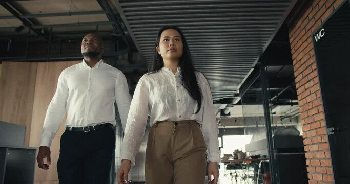 Confident Asian brunette girl walks around the office, her multi-racial company joins the girl. Collaboration and teamwork in the office in a team
