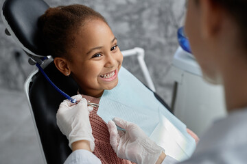 Portrait of cute black girl in dental chair with nurse or dentist preparing her for teeth exam, copy space